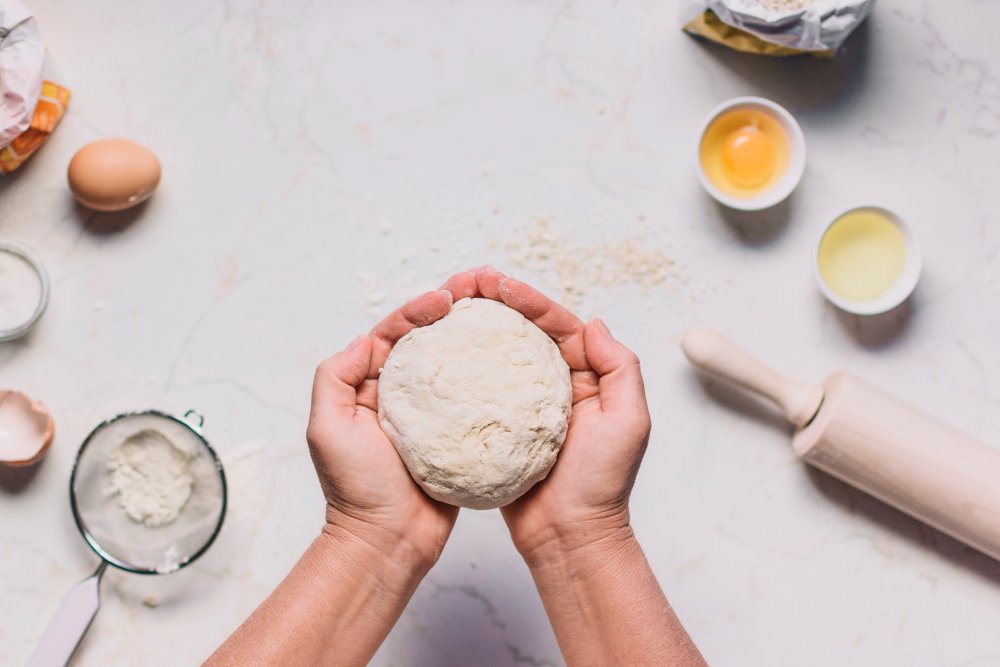 person-s-hand-holding-dough-with-baking-ingredients-kitchen-counter